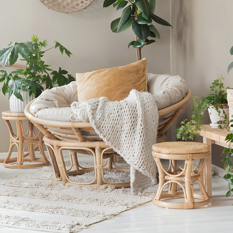 Loveuse en rotin avec un coussin gris et des tabourets en rotin avec des plantes en arrière plan